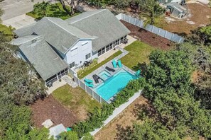 A two-story house with a swimming pool, surrounded by a fenced yard and trees. - Charming getaway in prime location with fast WiFi, W/D, and central AC (Bonita Springs)