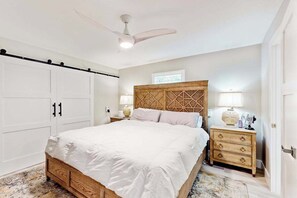Una camera da letto con un letto, una testiera in legno, un comodino, una cassettiera, una ventola a soffitto e un armadio.
