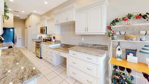 A kitchen with white cabinets, granite countertops, and a decorative shelf with flowers and a birdhouse. - Sail Away | Villa in Bonita Springs with pool access & water views (Bonita Springs)