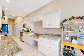 A kitchen with white cabinets, granite countertops, and a decorative shelf with flowers and a birdhouse. - Sail Away | Villa in Bonita Springs with pool access & water views (Bonita Springs)