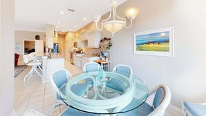 A modern kitchen with white cabinets, a dining area with a glass table and blue chairs, and a painting on the wall. - Sail Away | Villa in Bonita Springs with pool access & water views (Bonita Springs)