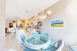 A modern kitchen with white cabinets, a dining area with a glass table and blue chairs, and a painting on the wall. - Sail Away | Villa in Bonita Springs with pool access & water views (Bonita Springs)