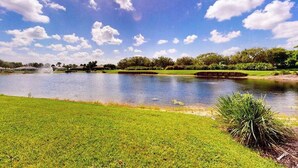 A serene landscape with a pond, grassy areas, and trees under a blue sky with clouds. - Sail Away | Villa in Bonita Springs with pool access & water views (Bonita Springs)