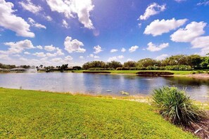 A serene landscape with a pond, grassy areas, and trees under a blue sky with clouds. - Sail Away | Villa in Bonita Springs with pool access & water views (Bonita Springs)