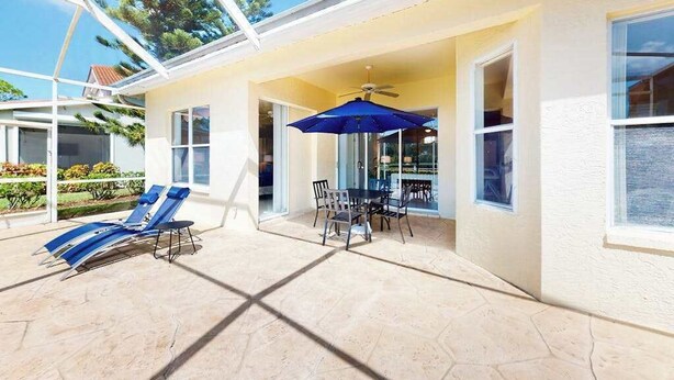 A covered patio area with lounge chairs, a table, and an umbrella. - Sail Away | Villa in Bonita Springs with pool access & water views (Bonita Springs)