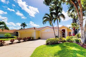 A residential house with a garage, a driveway, and a well-maintained lawn with palm trees. - Sail Away | Villa in Bonita Springs with pool access & water views (Bonita Springs)