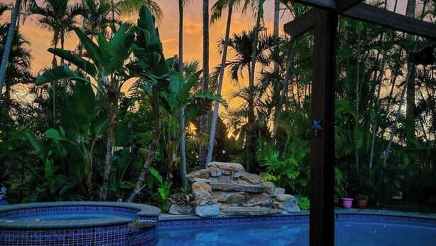 A pool surrounded by tropical plants and a stone structure. - Bali-inspired coastal home w/private pool, spa, and tiki room (Cape Coral)