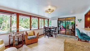 A spacious room with large windows, a dining area, and a view of greenery outside. - Bali-inspired coastal home w/private pool, spa, and tiki room (Cape Coral)