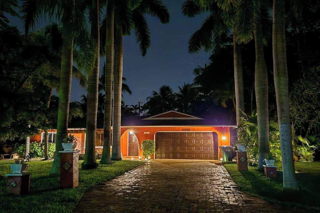 Una casa con garaje, rodeada de palmeras y un camino de entrada pavimentado.