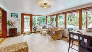 A spacious room with large windows, a ceiling fan, and a dining area with a table and chairs. - Bali-inspired coastal home w/private pool, spa, and tiki room (Cape Coral)