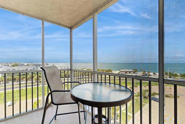 A balcony with a glass table and chairs, overlooking a coastal view. - Coastal beach studio with panoramic views, pool, and direct beach access (Bonita Springs)