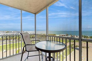 Ein Balkon mit Glastisch und -stühlen, der Blick auf die Küste freigibt.