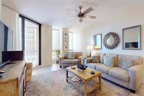 A living room with a sofa, coffee table, TV, and ceiling fan. - Stylish Water-View Condo w/ Balcony, Multiple Pools & Tennis Courts (Cape Coral)