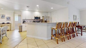 A modern kitchen with white cabinets, a central island, and a dining area with wooden chairs. - Canal-front Cape Coral oasis w/ private pool, hot tub & Dog friendly (Cape Coral)