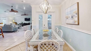 A dining area with a glass-top table, white wicker chairs, a chandelier, and a painting on the wall. - Canal-front Cape Coral oasis w/ private pool, hot tub & Dog friendly (Cape Coral)