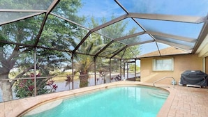 An indoor swimming pool with a glass ceiling, surrounded by trees and a brick patio. - Canal-front Cape Coral oasis w/ private pool, hot tub & Dog friendly (Cape Coral)
