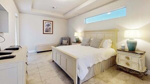 A bedroom with a large bed, two bedside tables with lamps, a chair, a dresser, and a framed picture on the wall. - Desirable SW Home | Private Heated Saltwater Pool | Newly Built in 2019 (Cape Coral)