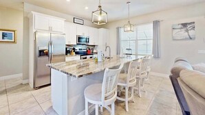 A modern kitchen with a central island, white cabinetry, stainless steel appliances, and pendant lighting. - Desirable SW Home | Private Heated Saltwater Pool | Newly Built in 2019 (Cape Coral)