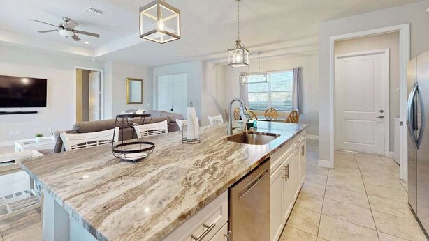 A modern kitchen with a marble countertop, stainless steel appliances, pendant lighting, and a dining area with a sofa. - Desirable SW Home | Private Heated Saltwater Pool | Newly Built in 2019 (Cape Coral)