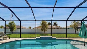 A swimming pool with a glass enclosure, a green umbrella, and a lawn with trees. - Desirable SW Home | Private Heated Saltwater Pool | Newly Built in 2019 (Cape Coral)