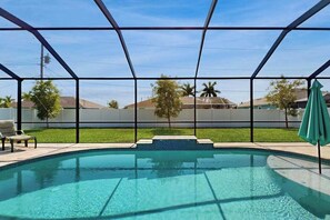 A swimming pool with a glass enclosure, a green umbrella, and a lawn with trees. - Desirable SW Home | Private Heated Saltwater Pool | Newly Built in 2019 (Cape Coral)
