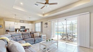 A modern living room with a sectional sofa, a glass coffee table, and a view of a pool through large sliding glass doors. - Desirable SW Home | Private Heated Saltwater Pool | Newly Built in 2019 (Cape Coral)