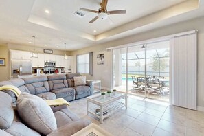 A modern living room with a sectional sofa, a glass coffee table, and a view of a pool through large sliding glass doors. - Desirable SW Home | Private Heated Saltwater Pool | Newly Built in 2019 (Cape Coral)