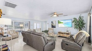 Ein Wohnzimmer mit einer Couch, einem Liegestuhl, einem Fernseher und einer Pflanze.