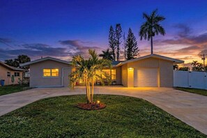 A residential house with a garage, a driveway, and a well-maintained lawn with a palm tree. - Updated Waterfront Escape | Dock & Easy Gulf Access | Walk to Beach & Tennis (Cape Coral)