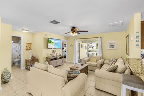 A living room with beige sofas, a television, and a ceiling fan. - Open-Air Waterfront Retreat | Private Pool (Cape Coral)