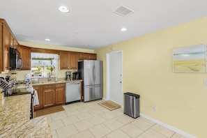 A kitchen with granite countertops, stainless steel appliances, wooden cabinets, a trash can, and a window with a view of the outdoors. - Open-Air Waterfront Retreat | Private Pool (Cape Coral)
