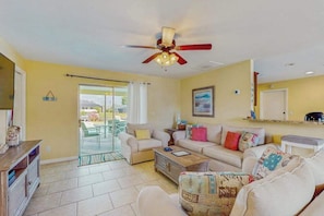 A living room with a ceiling fan, a sliding glass door leading to a patio, and a sofa set. - Serene Waterfront Retreat with Private Pool, Grill & Kayak Adventures (Cape Coral)