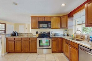A kitchen with wooden cabinets, a stainless steel oven, a microwave, and a dishwasher. - Serene Waterfront Retreat with Private Pool, Grill & Kayak Adventures (Cape Coral)