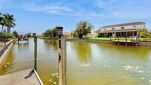 Un canal avec un quai en bois, un bâtiment doté d’un toit plat et un ciel dégagé.