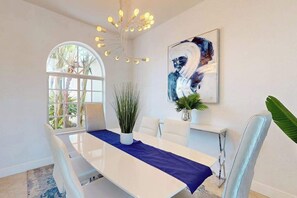 Une salle à manger moderne avec une table blanche, un chemin de table bleu et des chaises blanches.