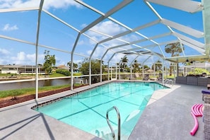 A swimming pool with a glass enclosure, surrounded by lounge chairs and a view of the landscape. - Waterfront home with heated pool, dock, & kayaks - minutes to beach (Cape Coral)