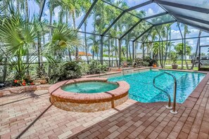 A covered outdoor swimming pool with a hot tub, surrounded by palm trees and a brick patio. - Wonderful cape home with private pool, furnished lanai, gas grill and WiFi (Cape Coral)