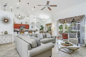 A spacious living room with a sofa, coffee table, and a dining area with a chandelier. - Wonderful cape home with private pool, furnished lanai, gas grill and WiFi (Cape Coral)