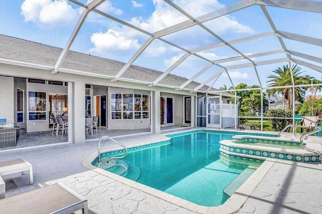 A covered outdoor swimming pool with a glass ceiling, surrounded by a patio area with seating and a poolside bar.