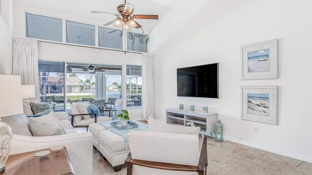 A spacious living room with a ceiling fan, large windows, a flat-screen TV, and a dining area with a table and chairs. - Stunning waterfront snowbird escape with private saltwater pool, dock, AC & W/D (Cape Coral)