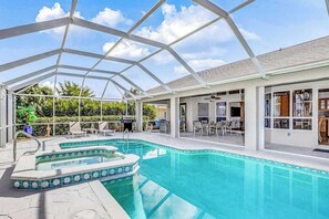 A covered outdoor swimming pool with a hot tub, lounge chairs, and a patio area. - Stunning waterfront snowbird escape with private saltwater pool, dock, AC & W/D (Cape Coral)