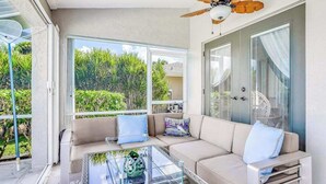 A modern living room with a glass coffee table, beige sofa, and a ceiling fan. - Stunning waterfront snowbird escape with private saltwater pool, dock, AC & W/D (Cape Coral)