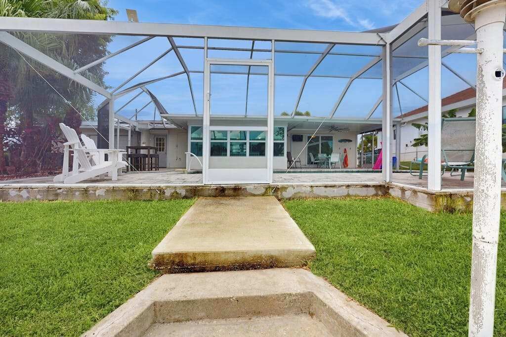 Un espacio al aire libre cubierto con un banco de hormigón, sillas blancas y un cerramiento de vidrio.