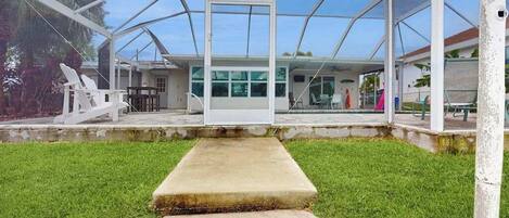 Un espacio al aire libre cubierto con un banco de hormigón, sillas blancas y un cerramiento de vidrio.