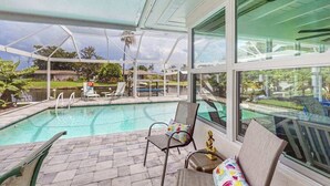 A covered outdoor swimming pool with lounge chairs and a view of the surrounding landscape. - Friendly Canalfront Home with Private Pool, High-Speed WiFi - Snowbird-Friendly (Cape Coral)