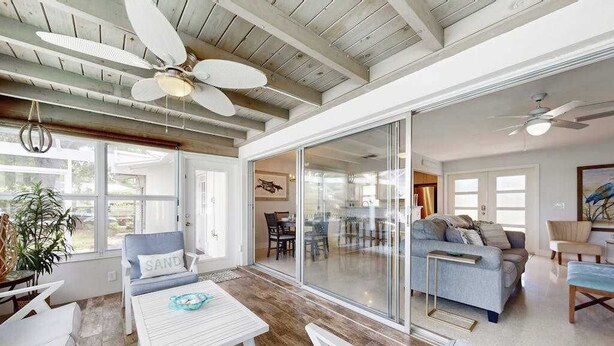 A spacious living area with a large sliding glass door, a ceiling fan, and a dining area with a table and chairs. - Friendly Canalfront Home with Private Pool, High-Speed WiFi - Snowbird-Friendly (Cape Coral)