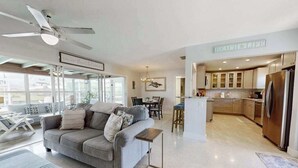 A modern living room with a grey sofa, a dining area, and a kitchen with wooden cabinets and a stainless steel refrigerator. - Friendly Canalfront Home with Private Pool, High-Speed WiFi - Snowbird-Friendly (Cape Coral)