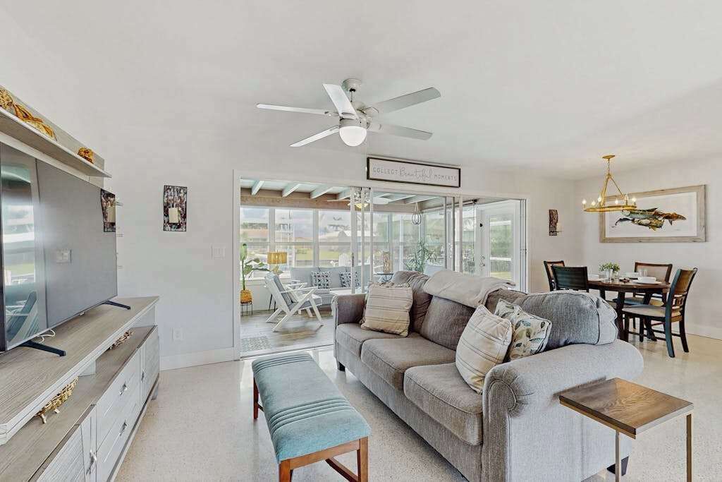 A living room with a sofa, a television, a ceiling fan, and a dining area with chairs and a table.
