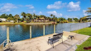 A waterfront view with a bench, a small pool, and palm trees. - Canal-Front Home with Private Pool and Dock, WiFi, and Pool Table (Cape Coral)