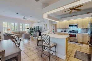 A spacious kitchen with a large island, modern appliances, and a dining area with a sofa and chairs. - Canal-Front Home with Private Pool and Dock, WiFi, and Pool Table (Cape Coral)